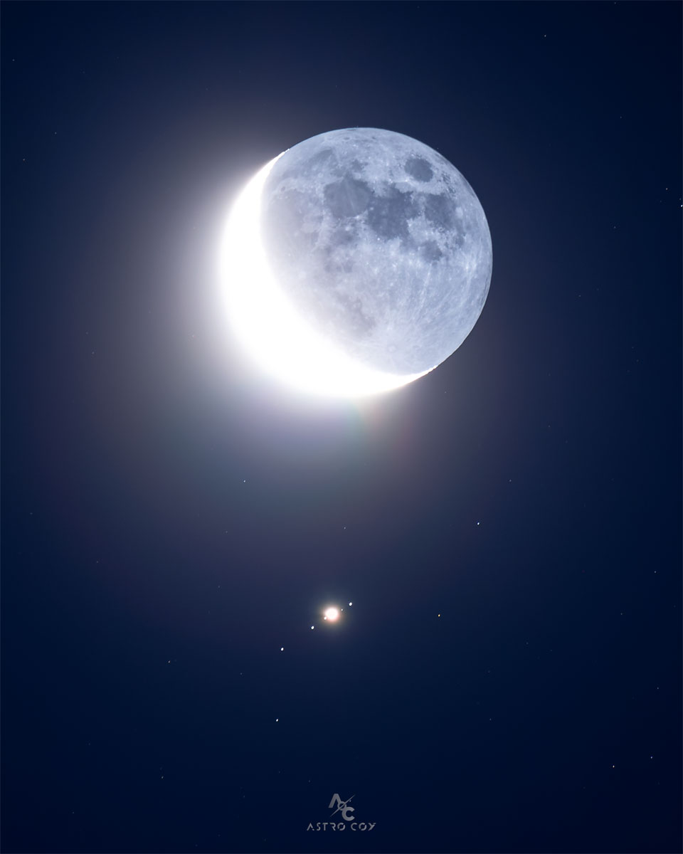 Earth Moon, in crescent phase, is seen just above the 
image centre. Directly below is a bright spot surrounded by
four other spots, all in a row, which are all moons of
Jupiter.
Please see the explanation for more detailed information.