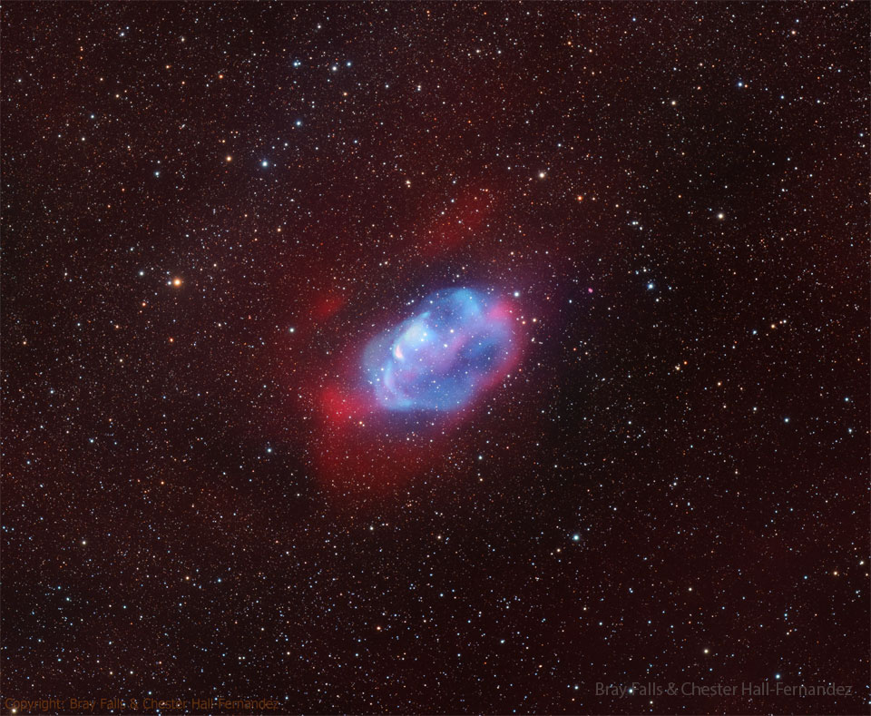 A diffuse nebula is seen against a dark starfield. The centre of the 
nebula is blue and it is surrounded by a red glow.
Please see the explanation for more detailed information.