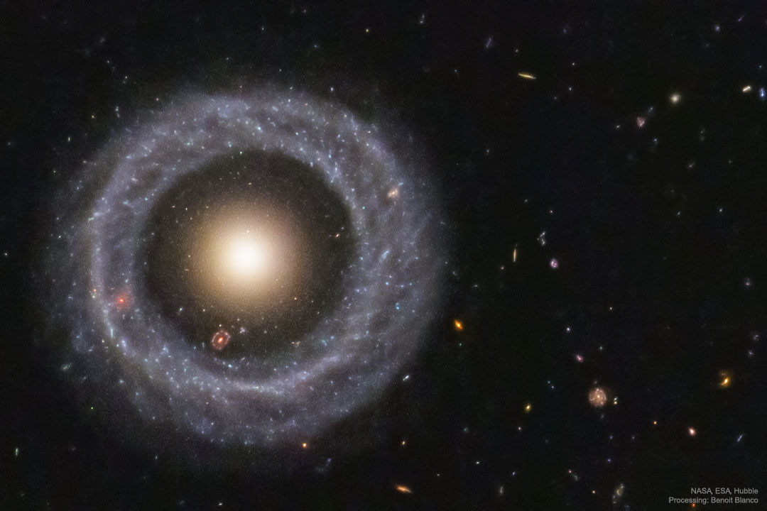 A nearly perfect circular ring of blue stars is seen
against a dark field of small background galaxies.
In the centre of the ring is a ball of yellow stars.
Please see the explanation for more detailed information.