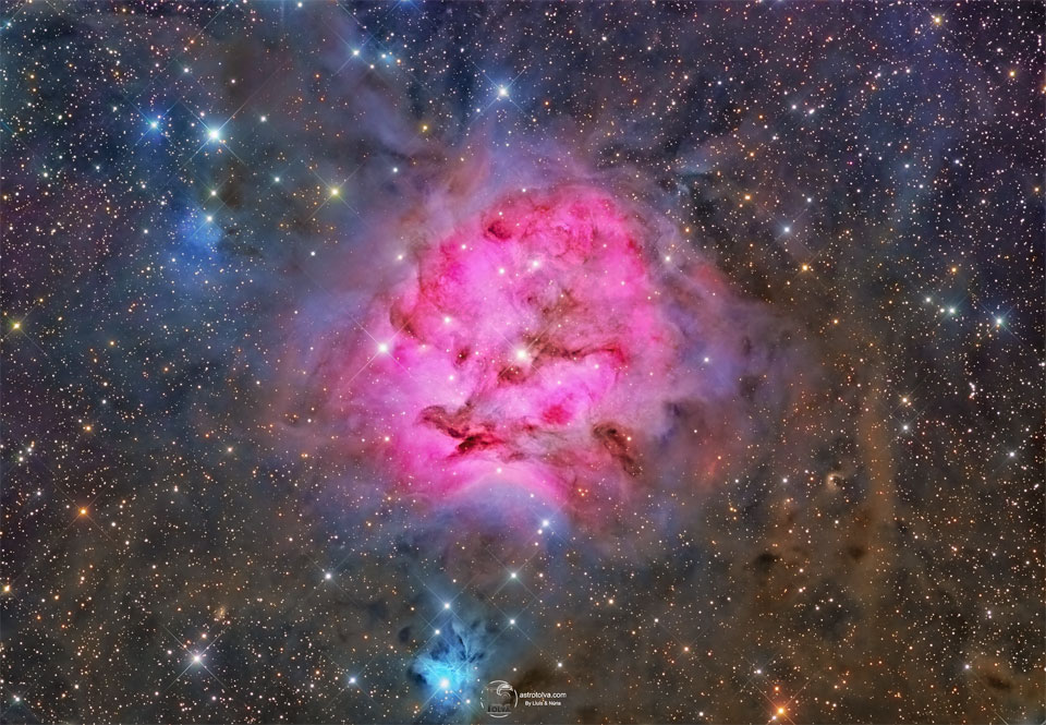 A red emission nebula is shown against a busy starfield 
with many dark dust filaments near the nebula's centre. 
Near the bottom of the image is a smaller blue reflection 
nebula. 
Please see the explanation for more detailed information.