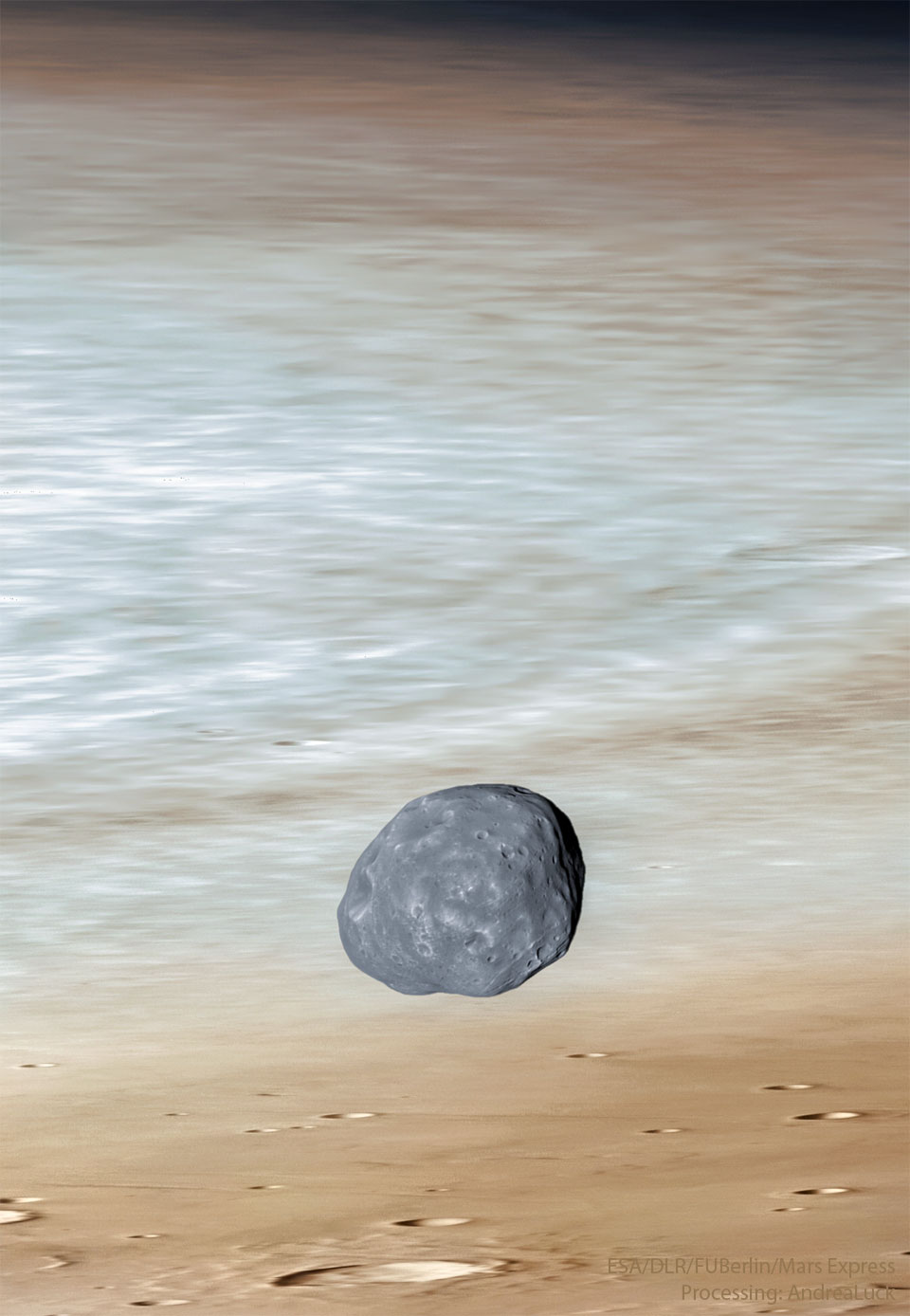 A dark irregularly-shaped moon is seen in front of the red
planet Mars. Craters are visible in the foreground and the edge
of the planet is just visible at the top of the image. 
Please see the explanation for more detailed information.