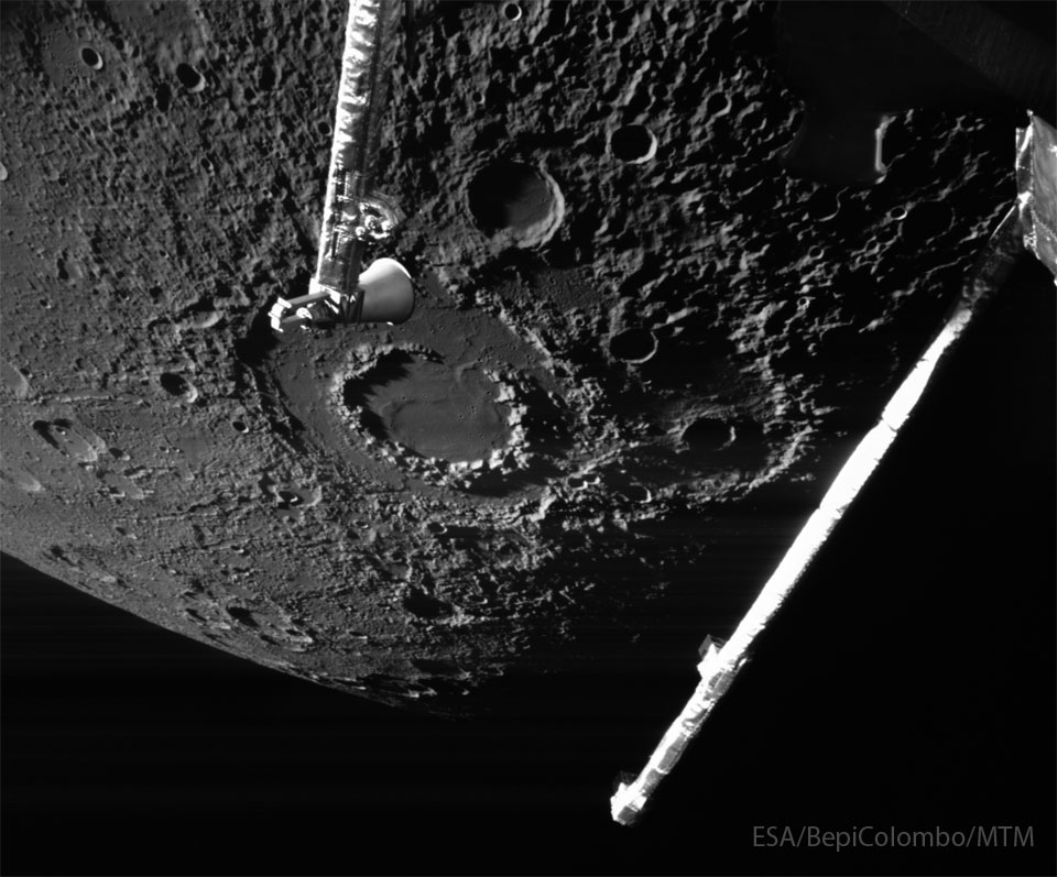 The cratered surface of a large body is shown: Mercury.
The largest feature visible is a large impact crater with two
rings, near the image centre. Arms from the BepiColumbo 
spacecraft that took the image are seen extending into the 
image from the top and the right. 
Please see the explanation for more detailed information.