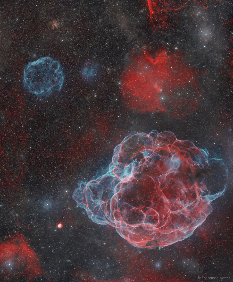 A star field appears that has several nebulae. Toward the upper
left is a angularly small supernova remnant coloured blue, while 
dominating the lower right is a large supernova remnant in both
red and blue. 
Please see the explanation for more detailed information.