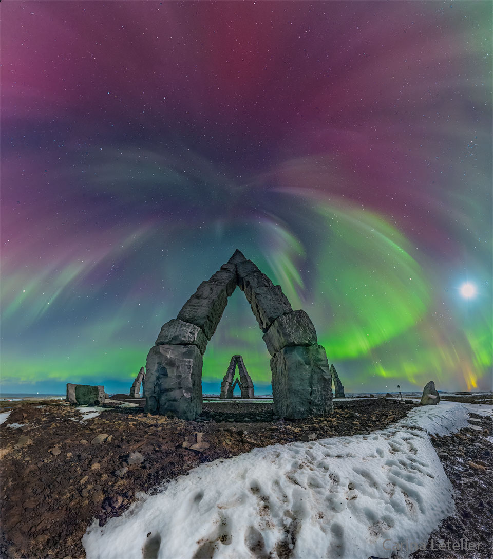 Multi-coloured aurora are seen above an unusual stone
gateway, the first of several similar gateways seen in
the distance. 
Please see the explanation for more detailed information.