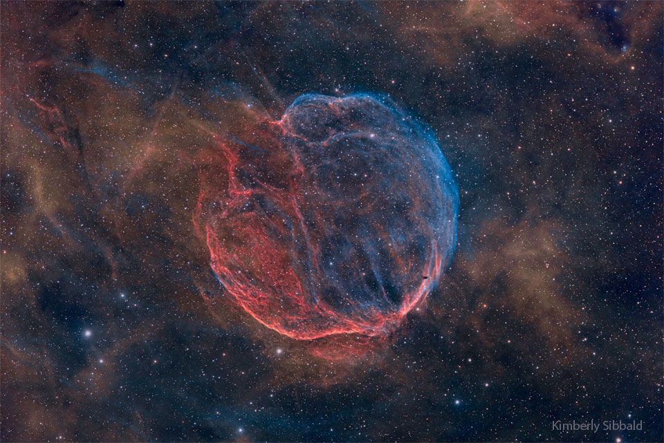 A nearly spherical but stringy nebula is shown against
a starry background. The nebula is coloured blue and red. 
Please see the explanation for more detailed information.