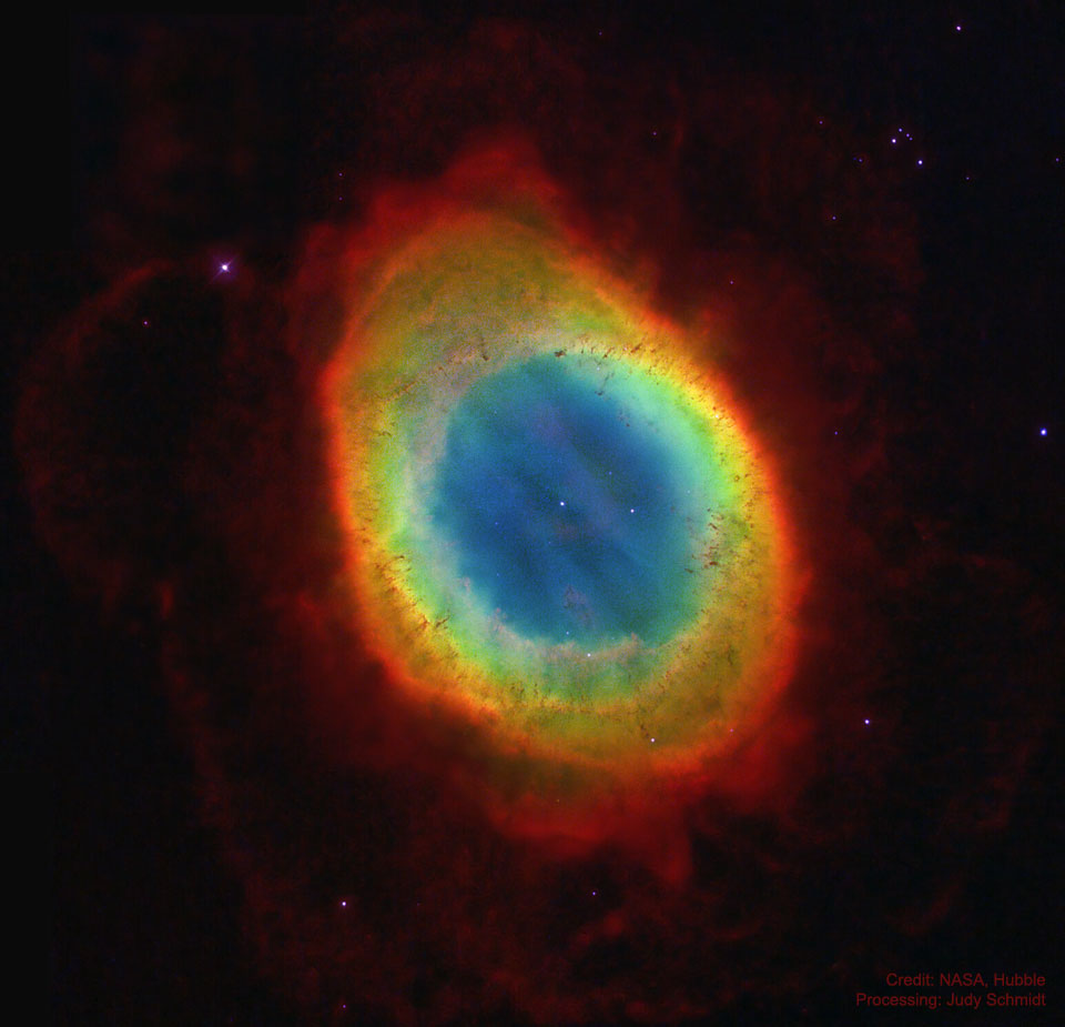 A colourful oval nebula is shown star field is shown 
in a sparse starfield. Fainter red nebulosity surrounds the
bright oval. A relatively bright star is seen in the oval's
centre.
Please see the explanation for more detailed information.
