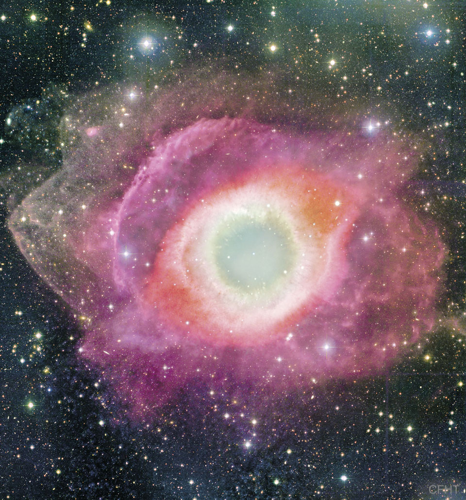 A colourful circular nebula is shown that is beige in the centre,
red further out, and gas violet rings even further out.
Please see the explanation for more detailed information.