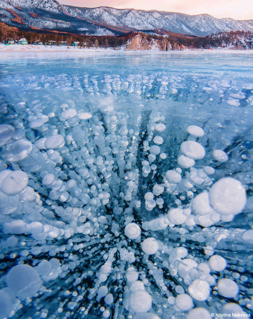 A frozen lake is shown that appears quite blue.
Many oval light-coloured bubbles are frozen into the 
ice, many times in columns. 
Please see the explanation for more detailed information.