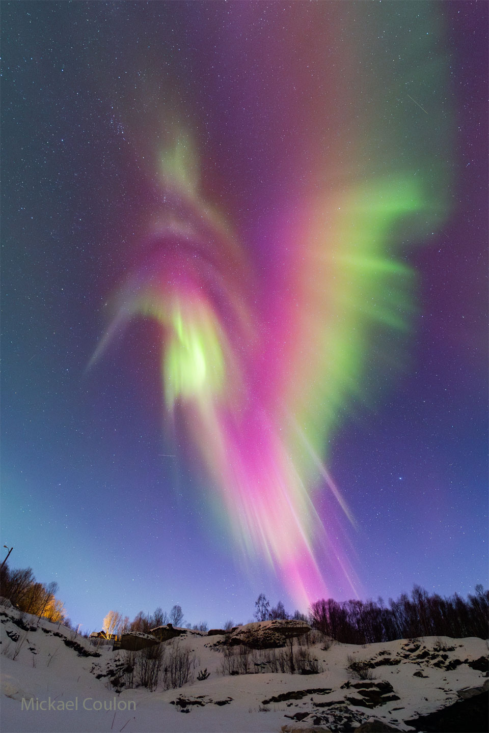 A snowy landscape sits below a star filled sky. 
Dominating the frame is a large aurora in red, green,
yellow, purple, white. 
Please see the explanation for more detailed information.