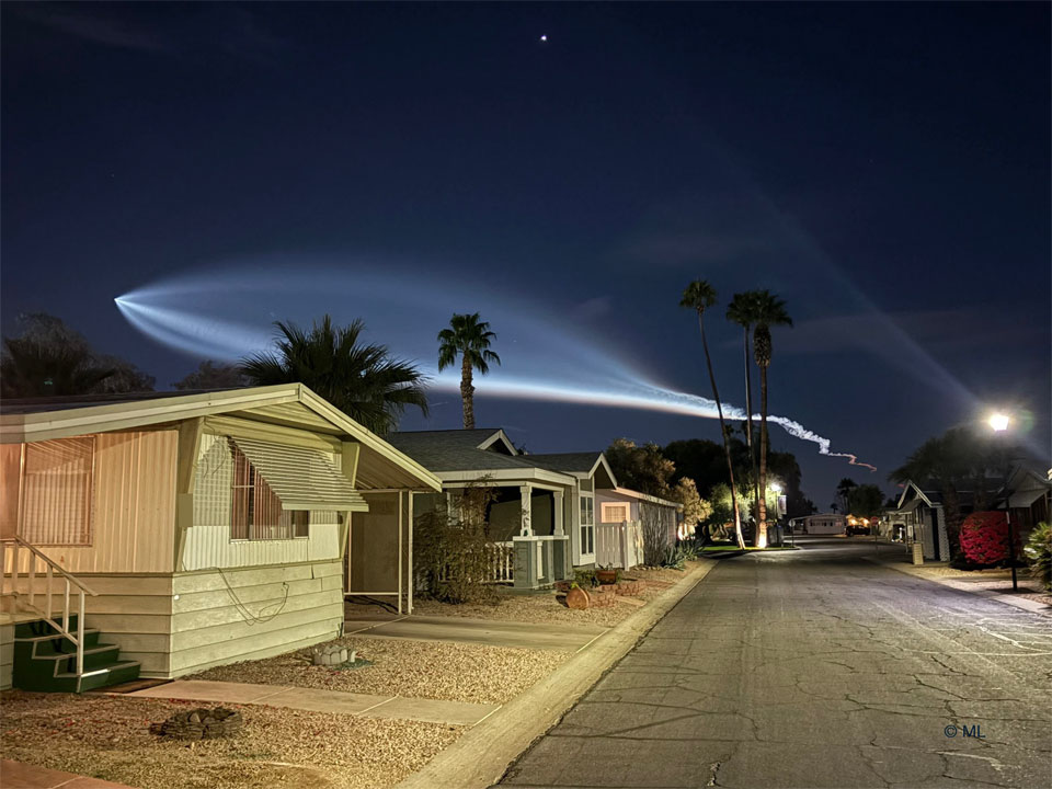 Houses are seen on a street below the night sky.
In the sky is a bright light plume that looks like the outline
of a giant fish. 
Please see the explanation for more detailed information.