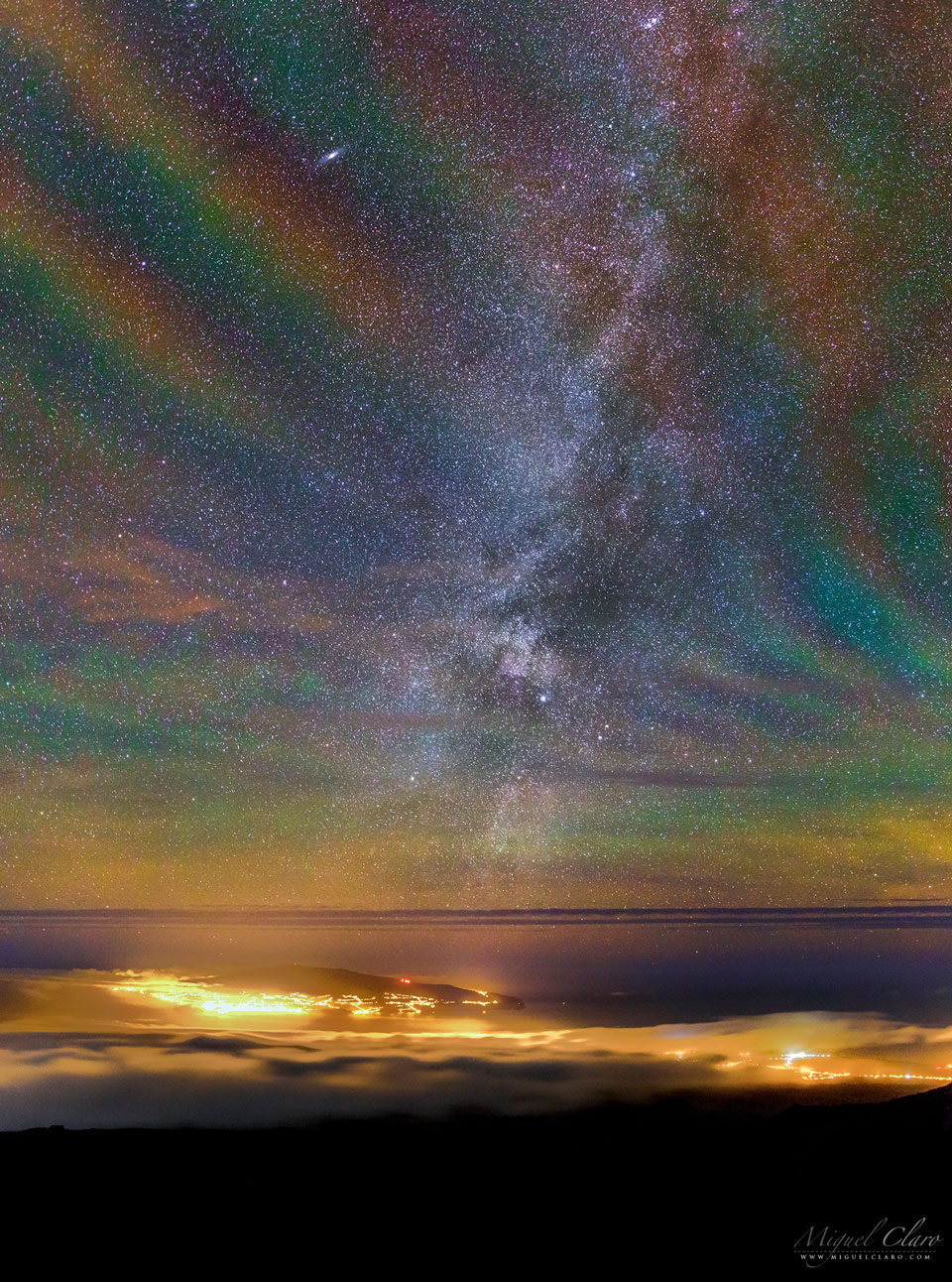 A starfield is seen over water, clouds, and the lights of
a city below. The starfield is oddly not black, but shows a 
repeating assortment of transparent colours diagonally from the lower
left to the upper right. 
Please see the explanation for more detailed information.