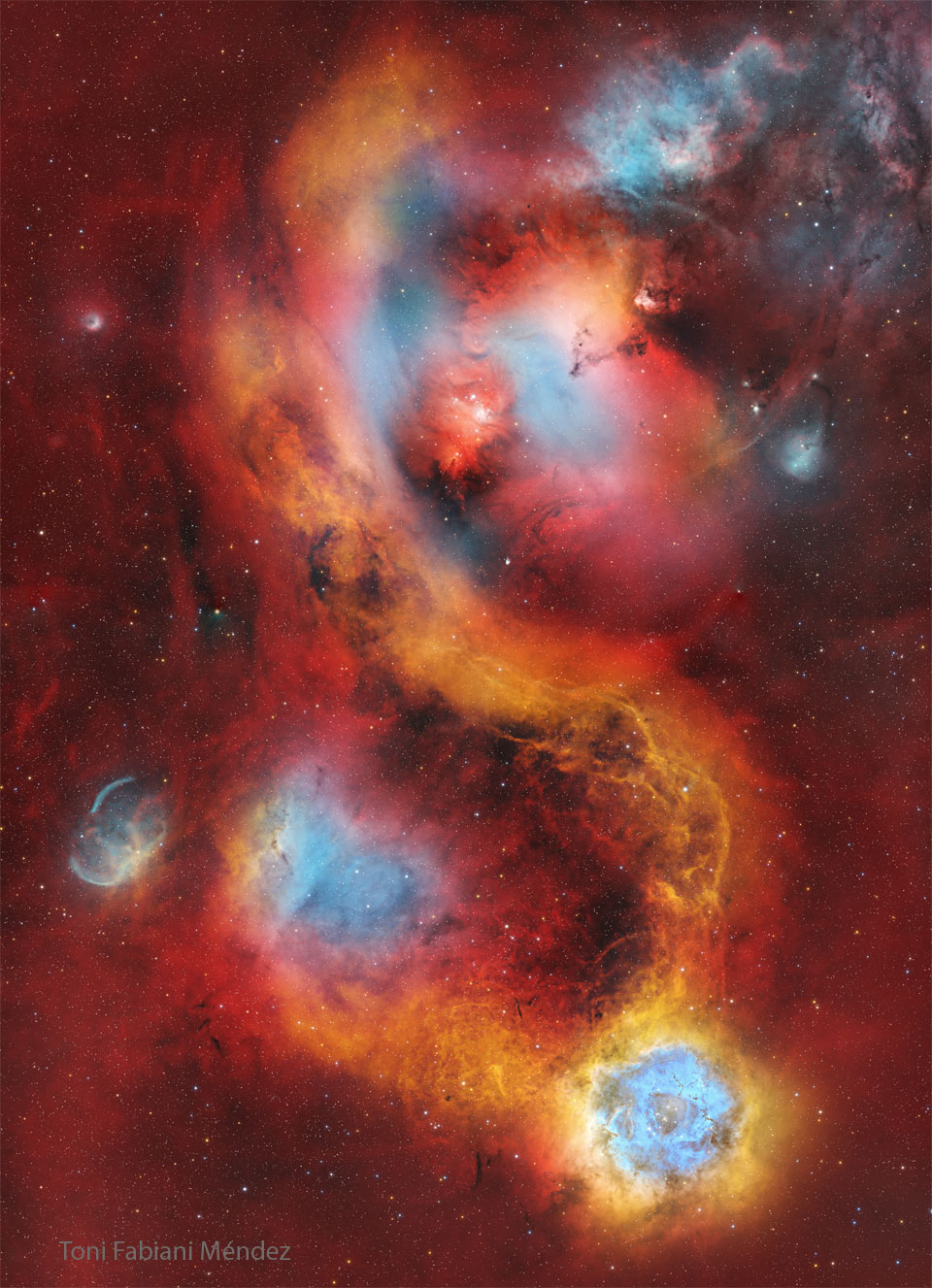A starfield is covered with a light red glow. Several
nebulae are seen near the centre. The famous Rosette nebula
appears in blue and white near the image bottom. 
Please see the explanation for more detailed information.