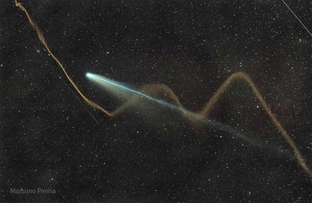 A dark sky shows bright comet with its tails extending
diagonally from the lower left. Two tails are visible for 
the comet -- a long blue tail and a shorter wider white tail.
Oddly, a wiggly tan stream appears to be a third tail -- but
is actually the dust from a dissipated meteor. 
Please see the explanation for more detailed information.