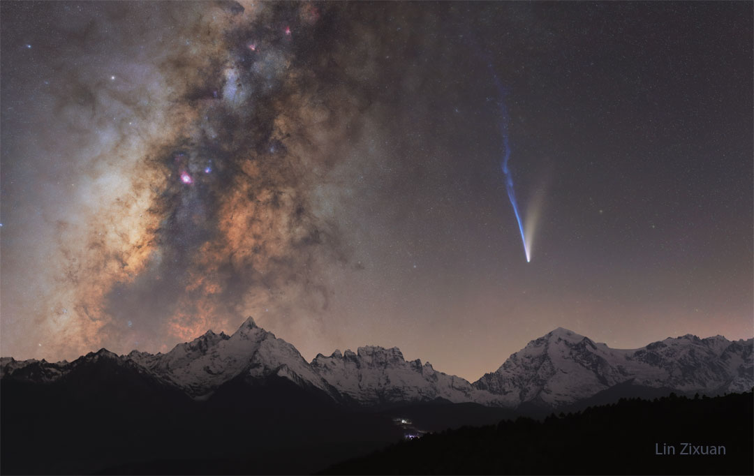 A night skyscape is shown over snowcapped mountains.
On the left is the band of the Milky Way Galaxy, while
on the right is a bright comet with two tails -- a white
tail going up and trailing to the right and a longer blue
tail going up and trailing off to the left. 
Please see the explanation for more detailed information.