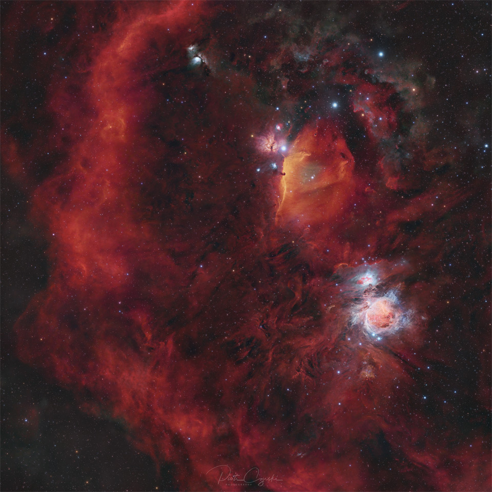 A starfield is shown filled with red glowing gas. On
the right is a blue-glowing complex nebula, while on the left
there is a long encircling arc of red gas. 
Please see the explanation for more detailed information.