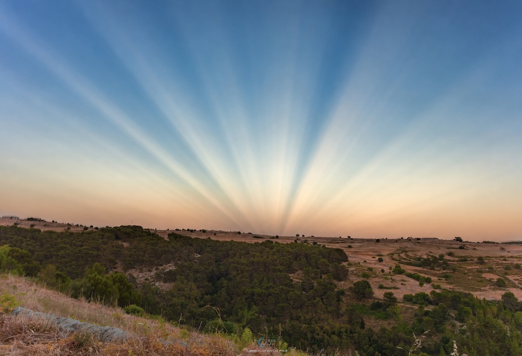 A landscape with an open horizon shows
	    sunset colour and coverging rays of light.