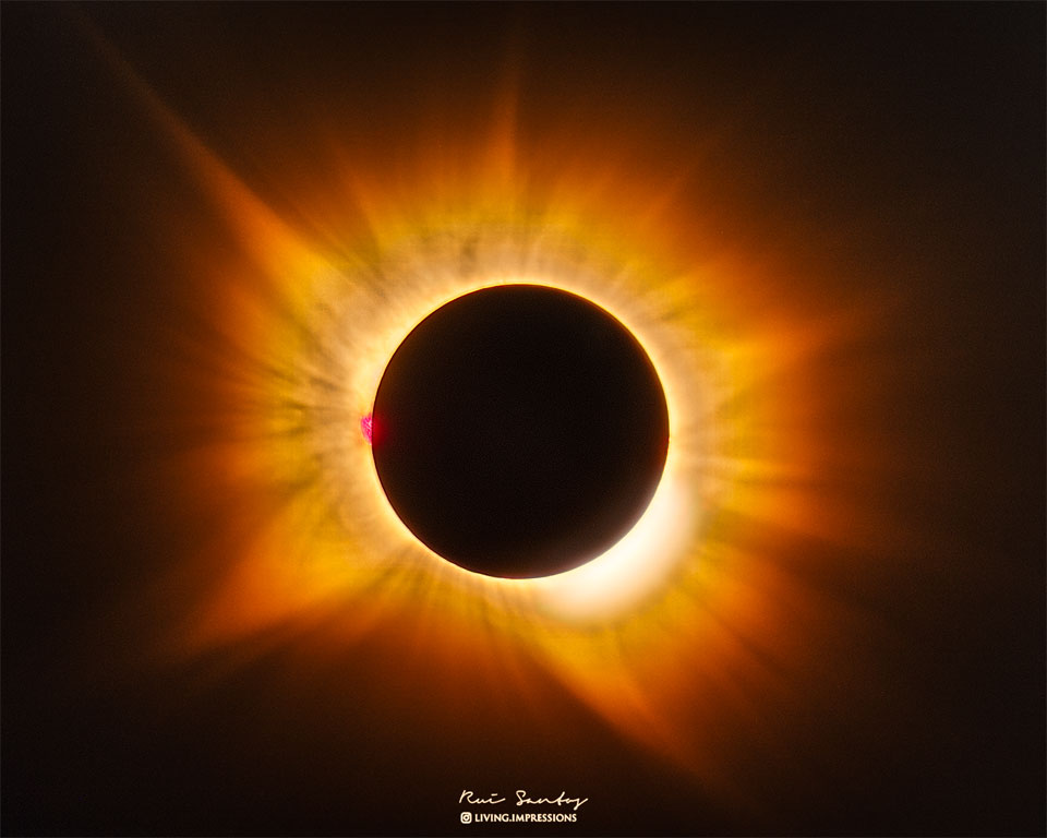 A total eclipse Sun is featured in the image centre.
Around the Sun is a filamentary gold-hued corona flowing
out in all directions. 
Please see the explanation for more detailed information.